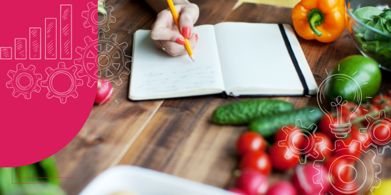 Imagem de um chef com prancheta analisando fichas técnicas de pratos e bebidas gourmet em uma cozinha de restaurante.