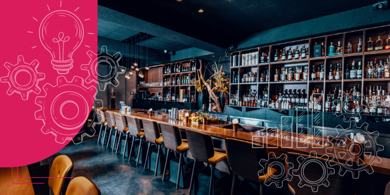 Bar em casa moderno e sofisticado com balcão de mármore preto, banquetas altas, prateleira de madeira com garrafas variadas e frutas cítricas.