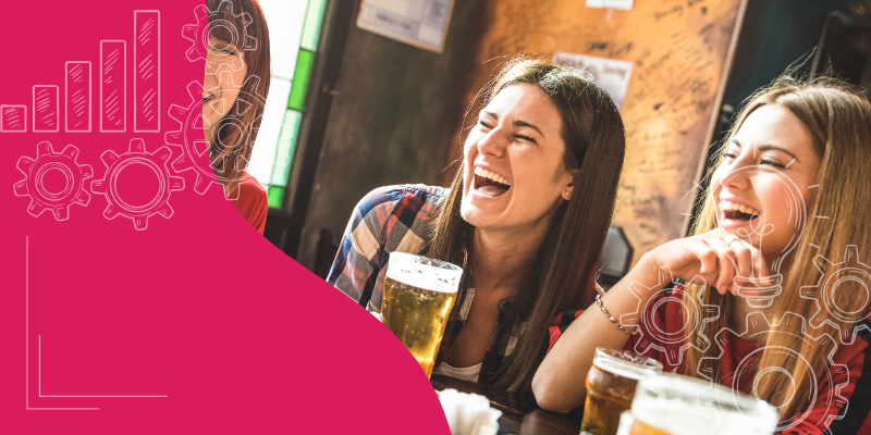 Grupo diversificado comemorando o Happy Hour em um bar moderno, brindando com coquetéis coloridos, iluminação aconchegante, enfatizando estratégias de alegria para clientes.