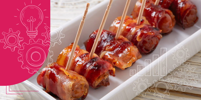 Imagem de uma mesa de restaurante com prato central de finger foods variados, incluindo mini sanduíches e canapés, em um ambiente sofisticado.
