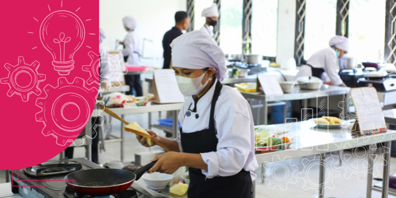 Cozinha de restaurante movimentada com chefs preparando pratos coloridos e utensílios de aço inoxidável.