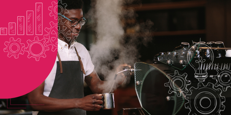 Barista preparando bebidas quentes num café moderno com clientes ao redor do balcão de aço inoxidável.