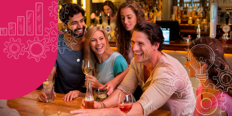 Pessoas se divertindo em um bar à noite, com coquetéis coloridos e lâmpadas Edison penduradas.